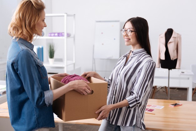 Kind young woman taking away a box from her colleague