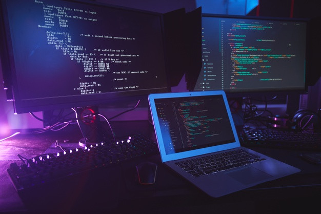 Various computer equipment with programming code on screens on table in dark room